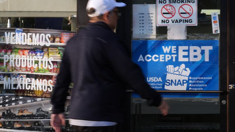 Un cliente pasa frente a una panadería con un letrero de información sobre el programa SNAP...